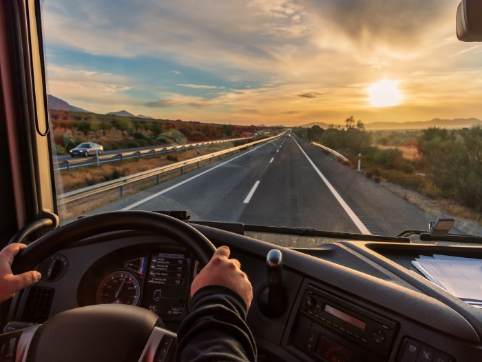 Truck driver behind wheel driving down the road during sunset.